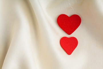 Red wooden decorative hearts on white silk background.