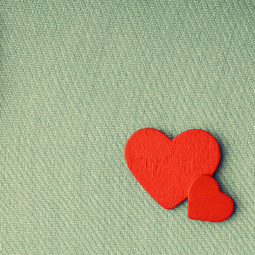 Red wooden decorative hearts on green cloth background.