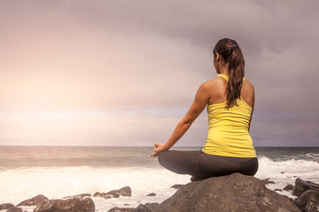 young woman practicing yoga meditation on the beach at sunset