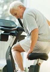 Senior man adjusting seat on a bike machine in a fitness club