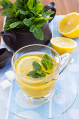 Teapot with mint and cup of tea on a wooden surface