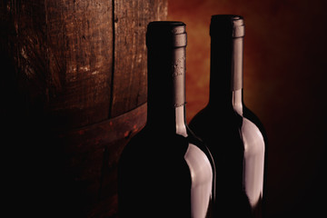 Red wine bottles and wooden barrel on warm background Fine wine tasting concept