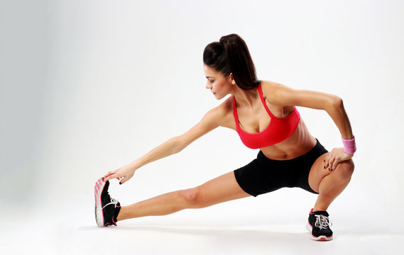 Young beautiful sport woman stretching legs on gray background