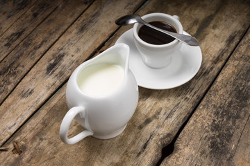 Coffee. Cup of Coffee with Milk Jug on Wood Background.