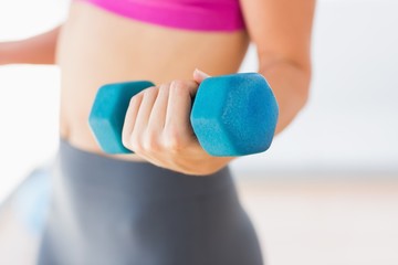 Mid section of a woman lifting dumbbell weight in gym - Powered by Adobe