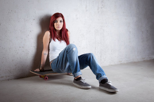 Woman with skateboard portrait against concrete wall.