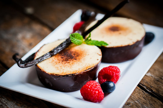 Creme brulee with vanilla sticks and berries on wooden backgroun