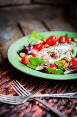 Baked seabass with tomatoes and basil on rustic wooden backgroun