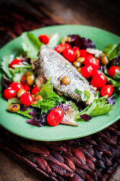 Baked seabass with tomatoes and basil on rustic wooden backgroun