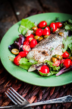 Baked seabass with tomatoes and basil on rustic wooden backgroun
