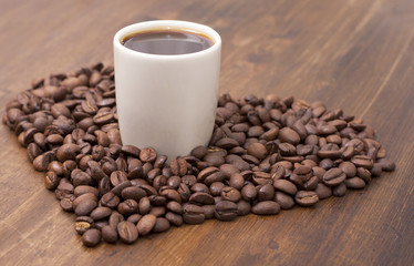 Heart of roasted coffee beans, a cup of coffee on a wooden table