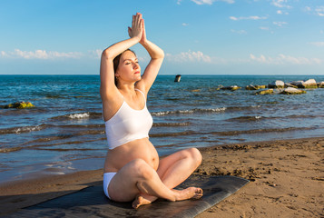 Fototapeta na wymiar Pregnant woman in sports bra doing exercise on yoga pose