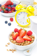 breakfast with granola, fresh berries, milk,  yellow alarm clock