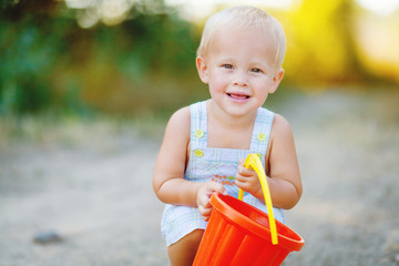 Little smiling boy with toy bucket outdoors