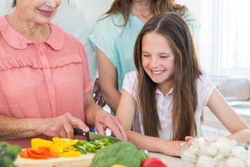 Obraz na płótnie Canvas Girl looking at grandmother cutting vegetables