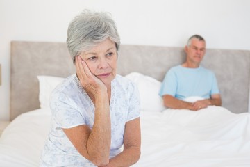 Fototapeta na wymiar Sad senior woman on bed with husband in background