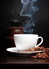 Coffee cup with smoke, grinder and grain against black wall.