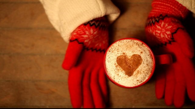 Hands in mittens holding hot cup of coffee