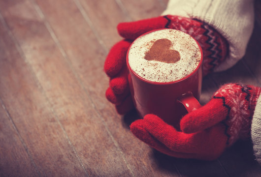 Hands in mittens holding hot cup of coffee