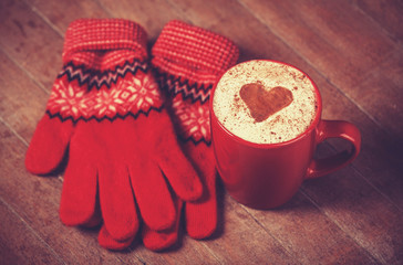 Gloves and cup with coffee and shape of the cacao heart on it.