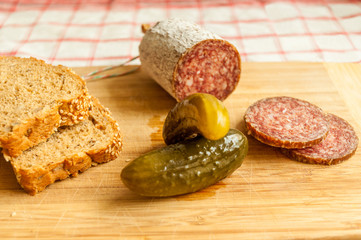 Salami slices with pickles on wood background