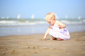 Fototapeta na wymiar Cute baby girl plays on the beach drawing on the sand