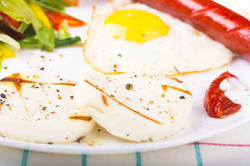 Fried egg and sausage on the plate with green salad and cheese