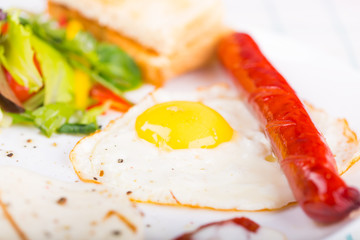 Fried egg and sausage on the plate with green salad and toasts
