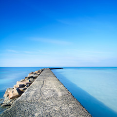 Concrete and rocks pier or jetty on blue ocean water