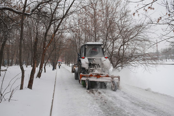 Fototapeta na wymiar snow-removal tractor cleans alley in the park