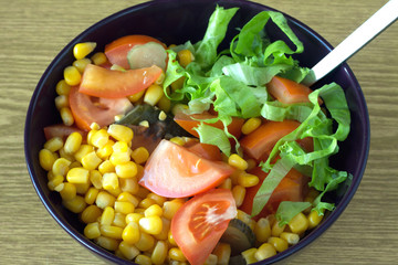 Vegetable salad in purple bowl on wooden surface closeup