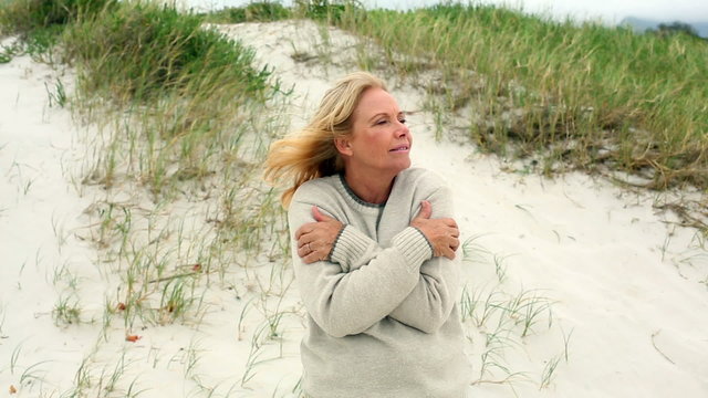 Smiling retired woman shivering on the beach