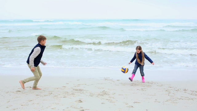 Siblings playing football on the beach