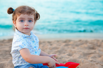 Blu eyes brunette toddler girl playing with sand in beach