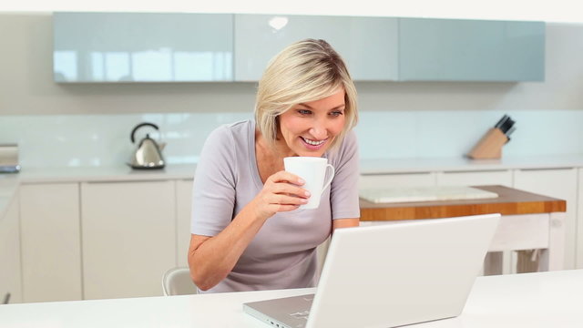 Blonde woman drinking coffee while using her laptop