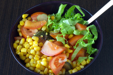 Vegetable salad in purple bowl on dakr wooden surface closeup