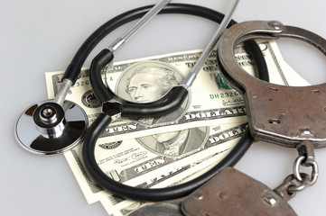 Stethoscope, handcuffs and money on gray