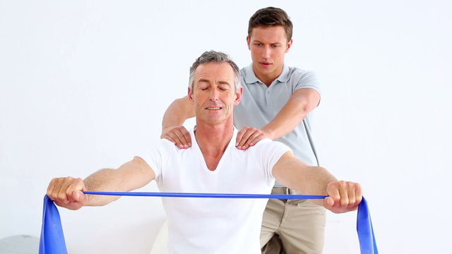 Physiotherapist watching patient stretching blue resistance band