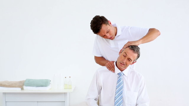 Physiotherapist giving stressed businessman a neck massage