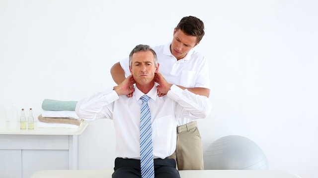 Businessman getting his shoulders checked by physiotherapist