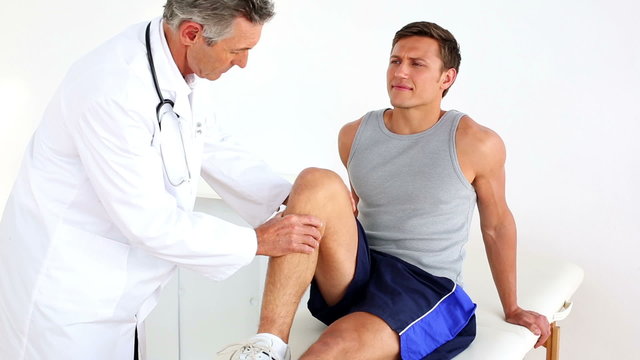 Mature doctor checking sportsmans injured knee