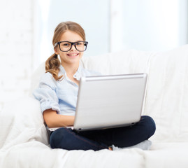 smiling girl in specs with laptop computer at home