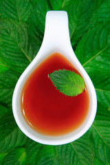 white cup of tea on a background of green leaves