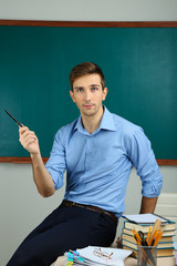 Young teacher sitting on desk in school classroom