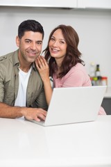 Fototapeta na wymiar Portrait of a happy couple using laptop in kitchen