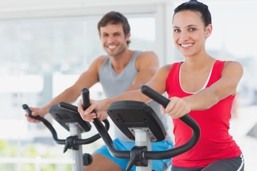 Obraz premium Smiling young couple working out at spinning class