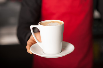 Hands of waiter serving a cup of cappucino