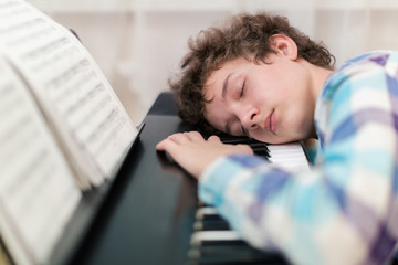 The boy has fallen asleep on the piano