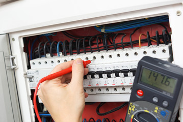 Hand of an electrician with multimeter probe at an electrical sw - obrazy, fototapety, plakaty