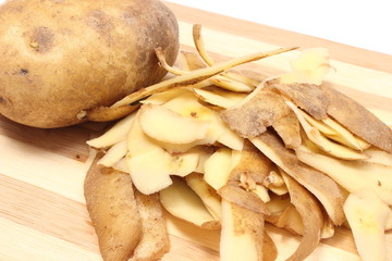 Whole potato and peels lying on wooden cutting board